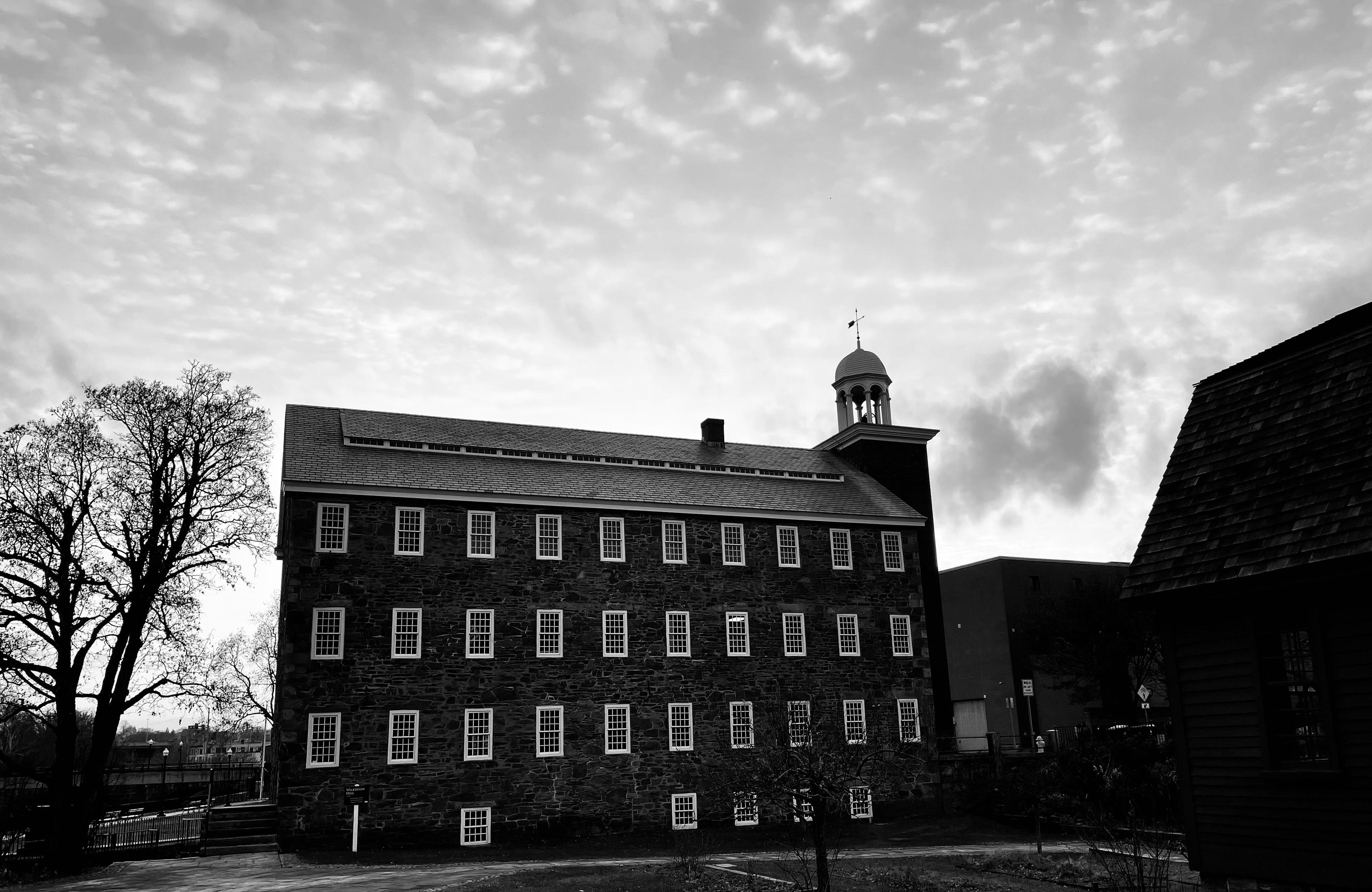 Picture of large 4 story stone mill with bell tower. Black and white photograph