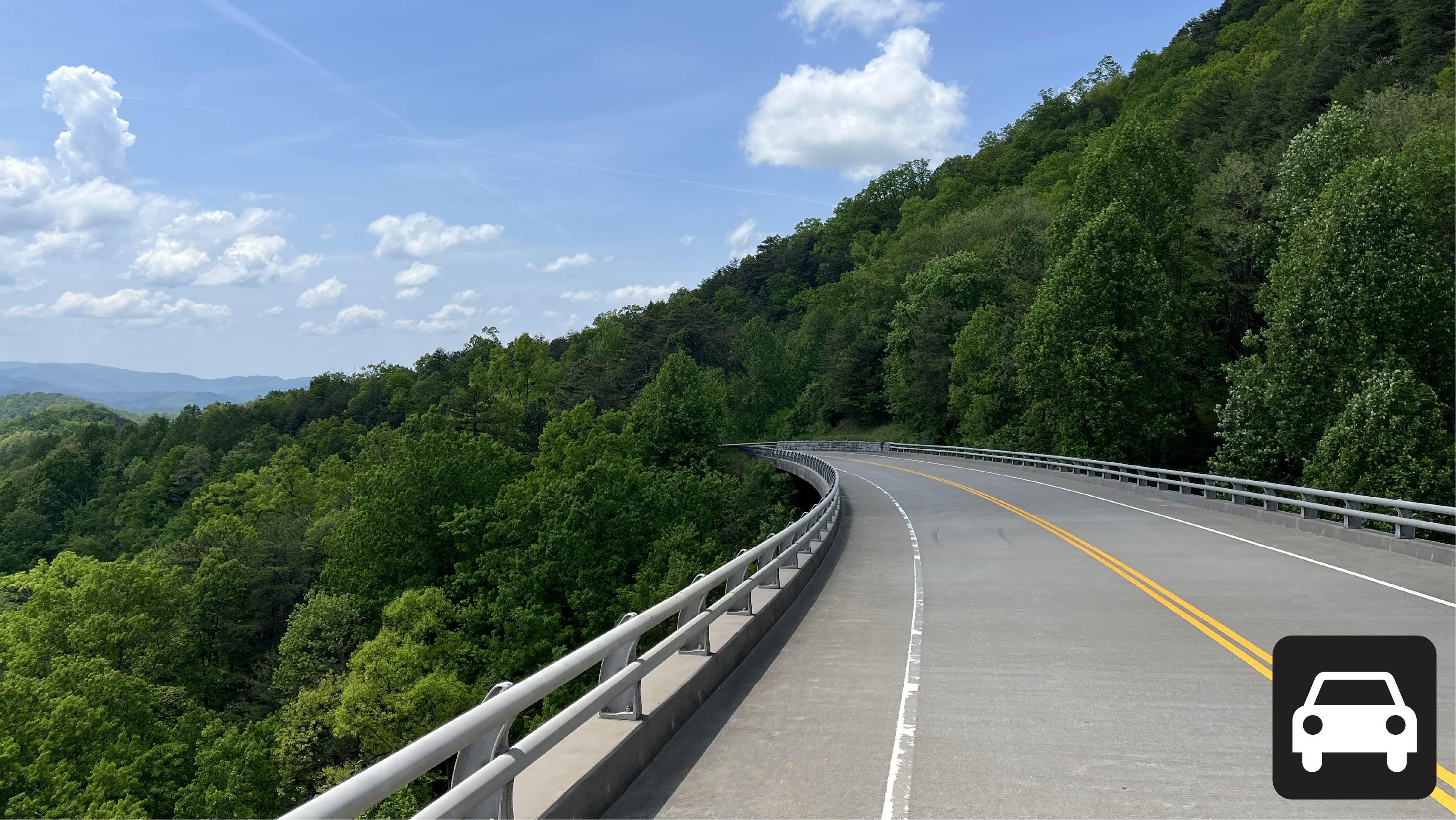 A roadway bridge with mountain views, the lower corner has a car icon.