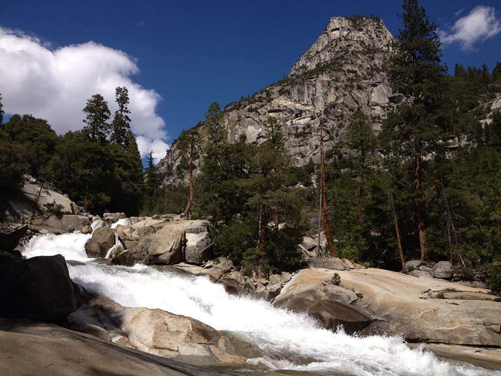 A cascading waterfall with massive granite mountains in the background.